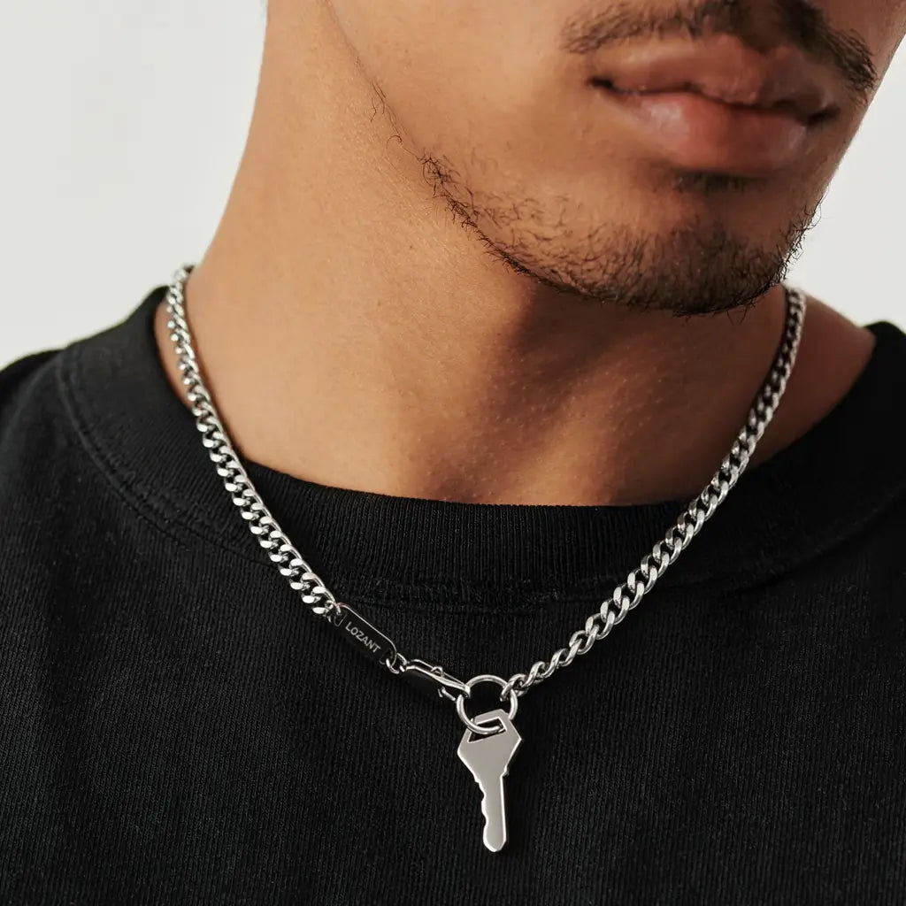 Black Male wearing a silver chain necklace featuring a key pendant.