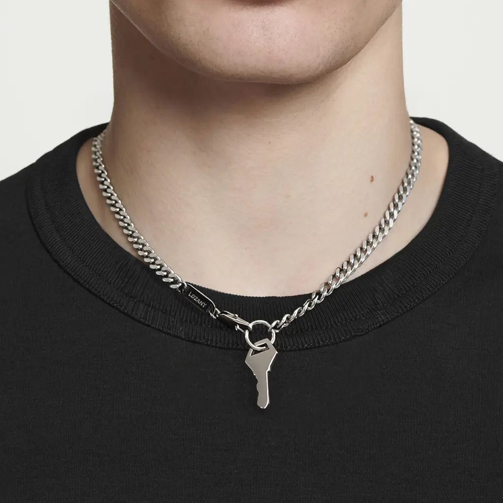 White Male wearing a silver chain necklace with a key pendant on a plain background